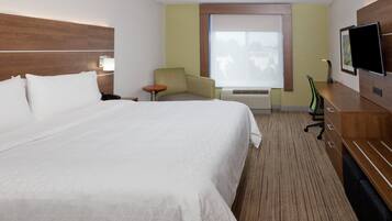 A hotel room with a large bed, a desk, a chair, a television, and a window with blinds.