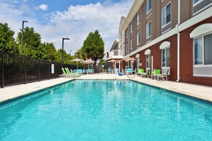 A swimming pool with lounge chairs and umbrellas, surrounded by a fence and trees.