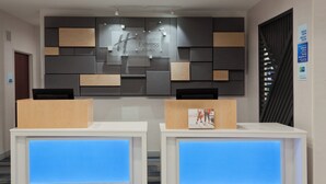 A reception area with two reception desks, a wall-mounted sign for Holiday Inn Express & Suites, and a check-in schedule on the wall.