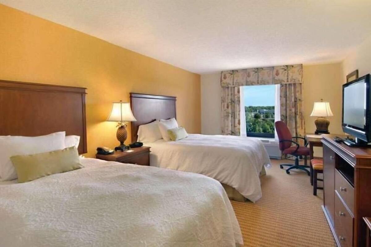 A hotel room with two beds, a television, a desk with a chair, and a window with a view.