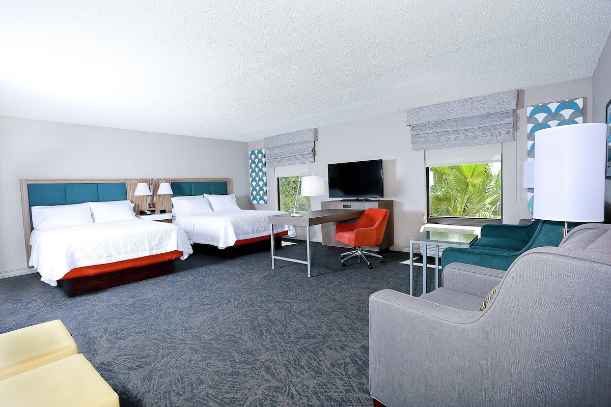 A hotel room with two beds, a desk, a TV, and a sofa.