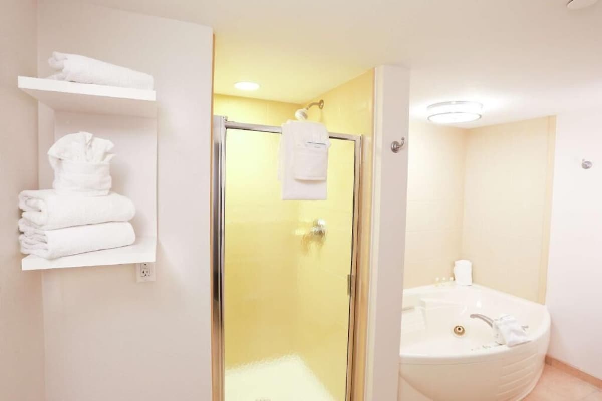 A bathroom with a glass shower enclosure, a white bathtub, and a shelf with folded towels.