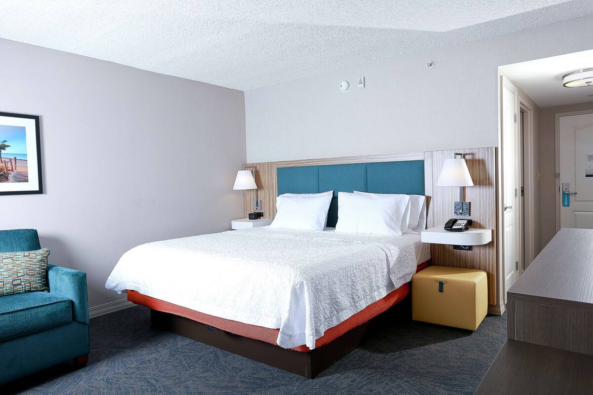 A hotel room with a bed, a nightstand, a chair, and a suitcase.