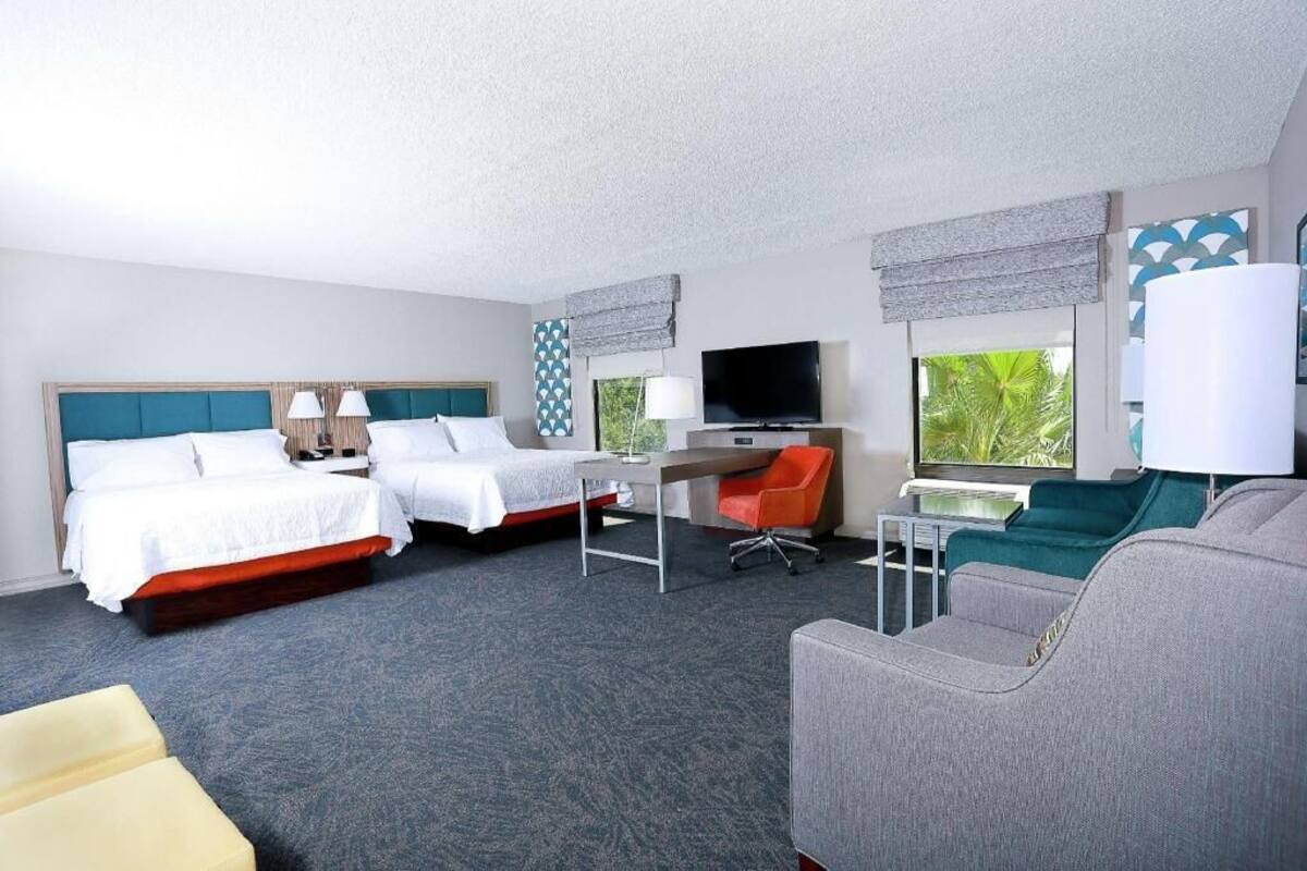 A hotel room with two beds, a desk, a TV, a sofa, and a window with a view.