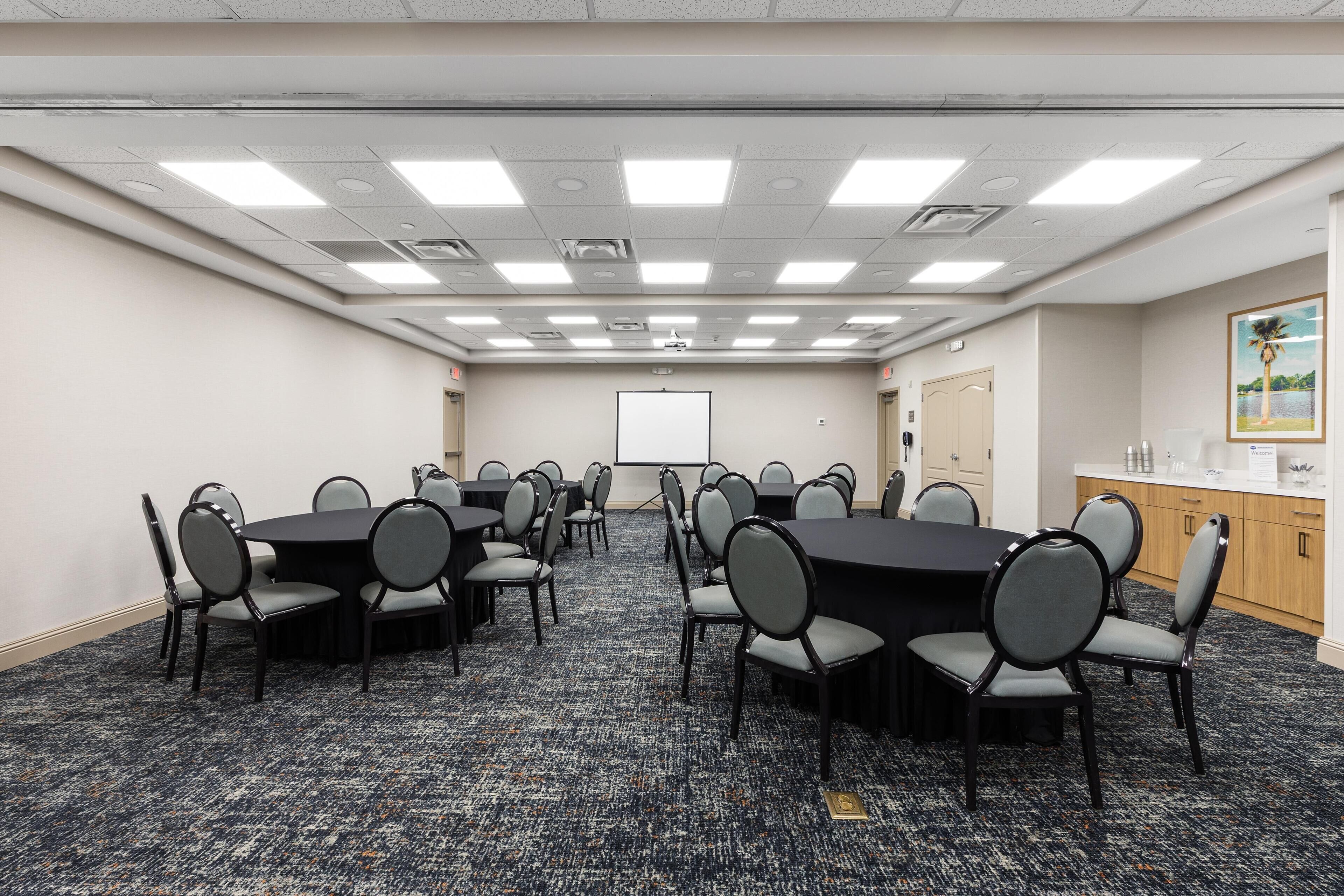 A conference room with multiple tables and chairs, a projector screen, and a whiteboard.