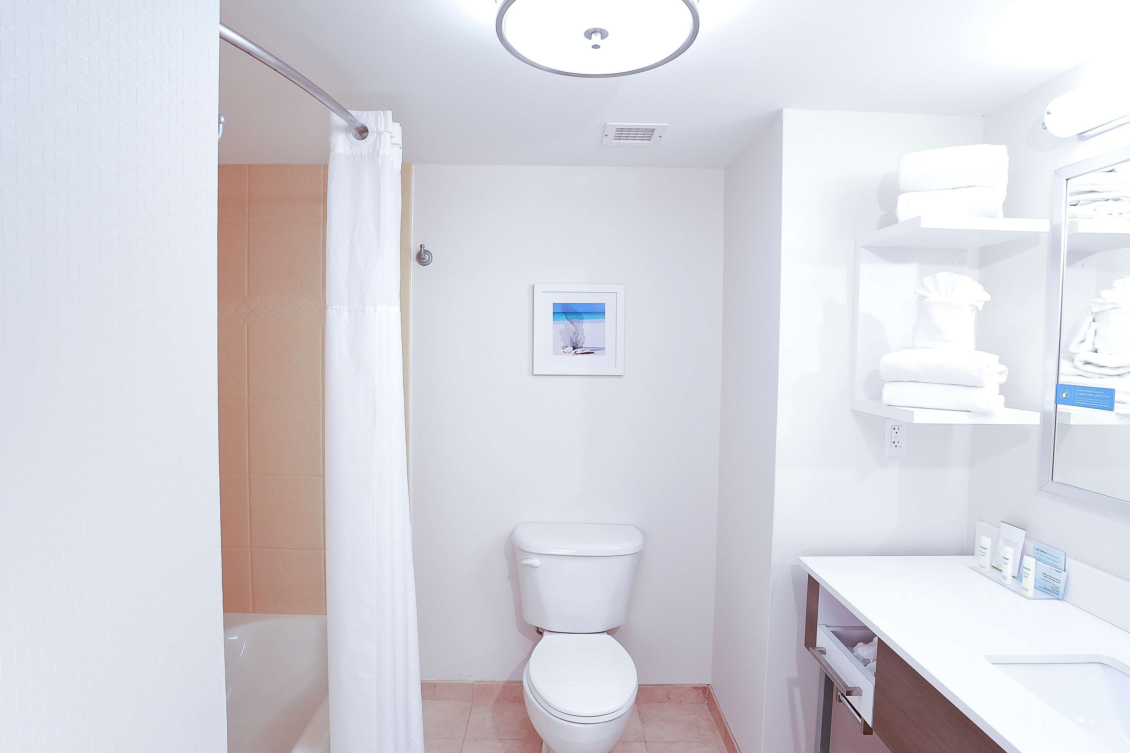 Ein Badezimmer mit Toilette, Dusche und Waschbecken inklusive Spiegel. An der Wand hängt ein gerahmtes Bild und ein Handtuchhalter mit Handtüchern.