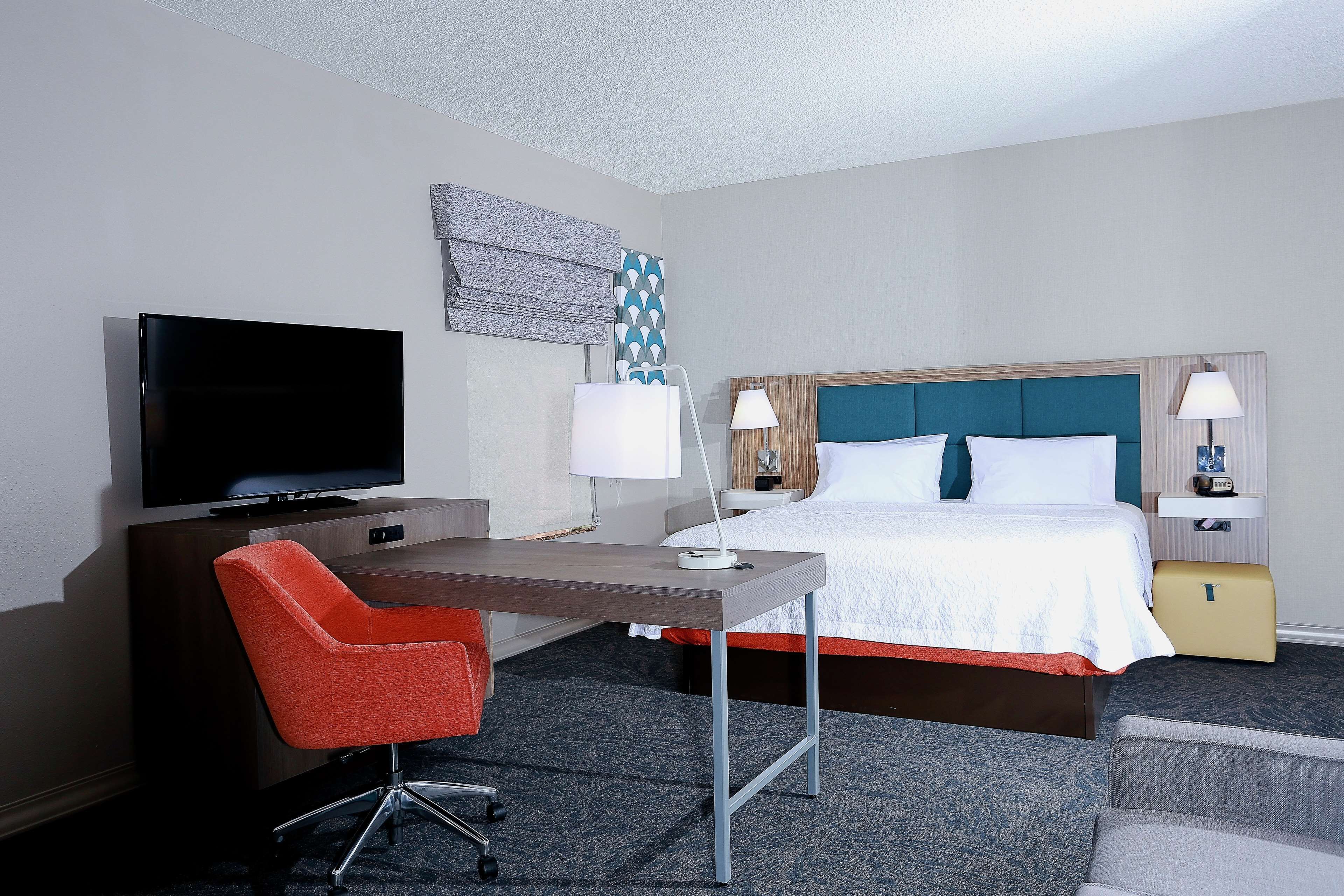 Habitación de hotel con cama, escritorio, silla, televisor y dos lámparas de noche.