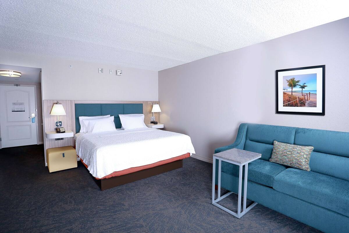 A hotel room with a bed, a sofa, a small table, and a framed picture on the wall.