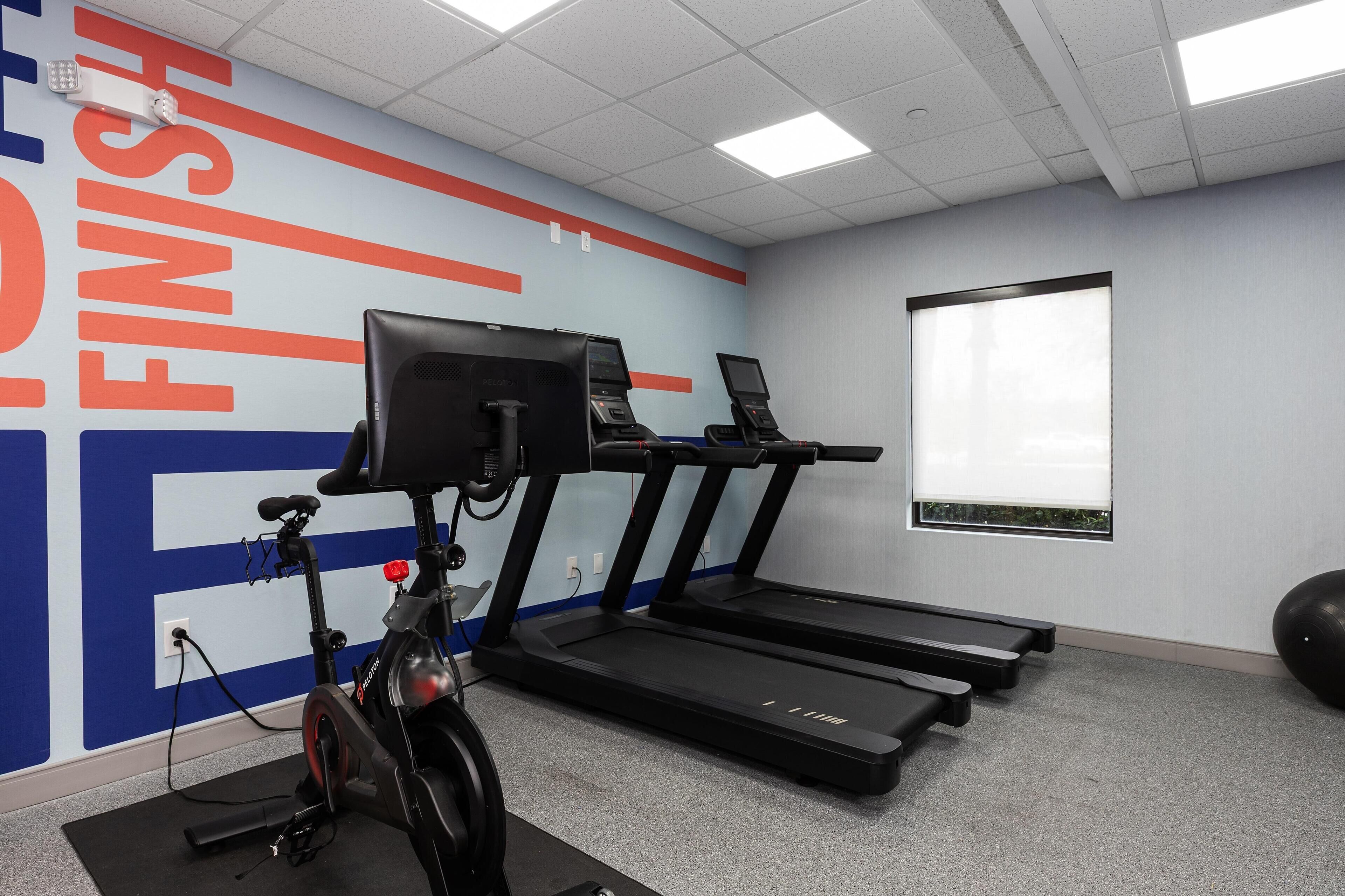 A fitness room with a stationary bike, two treadmills, and a large exercise ball.
