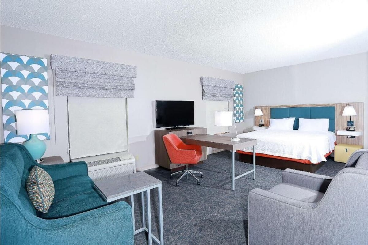 A hotel room with a bed, desk, TV, two chairs, and a small table.