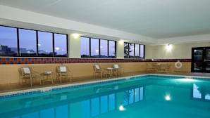 An indoor swimming pool with clear blue water, surrounded by lounge chairs and tables. - Hampton Inn & Suites Madisonville (Madisonville)