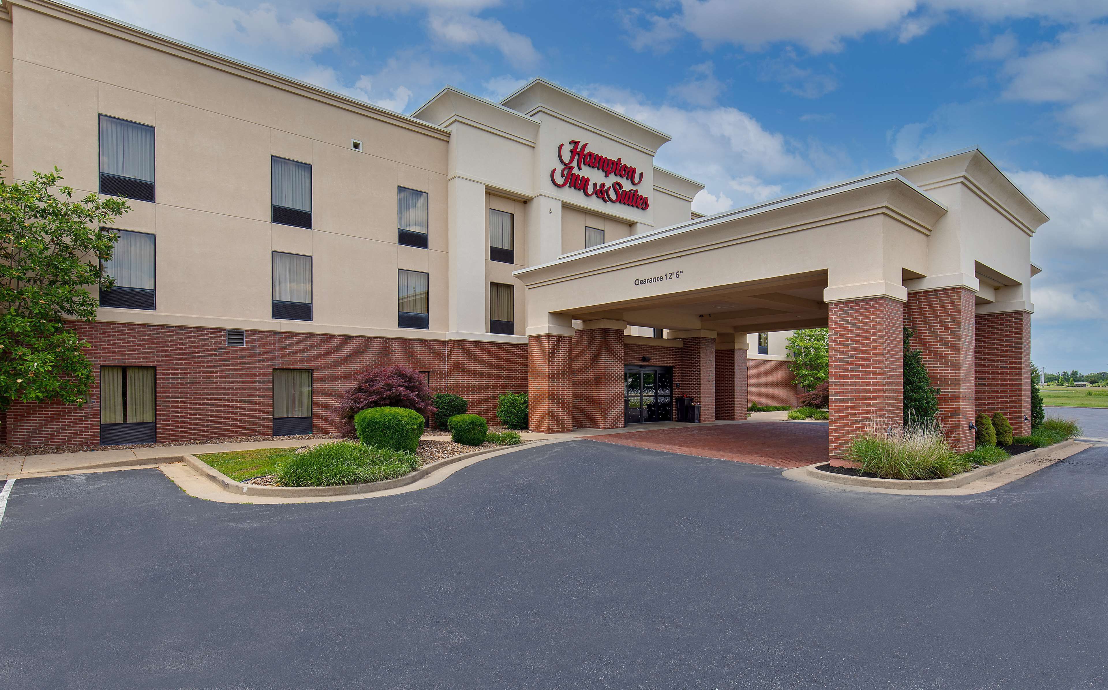 Ett Hampton Inn & Suites-hotell med en tydlig entré, en fasad av tegel och en parkeringsplats.