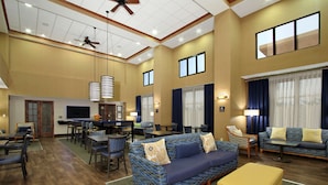 A spacious hotel lobby with a large sofa, dining area, and a ceiling fan. - Hampton Inn & Suites Madisonville (Madisonville)
