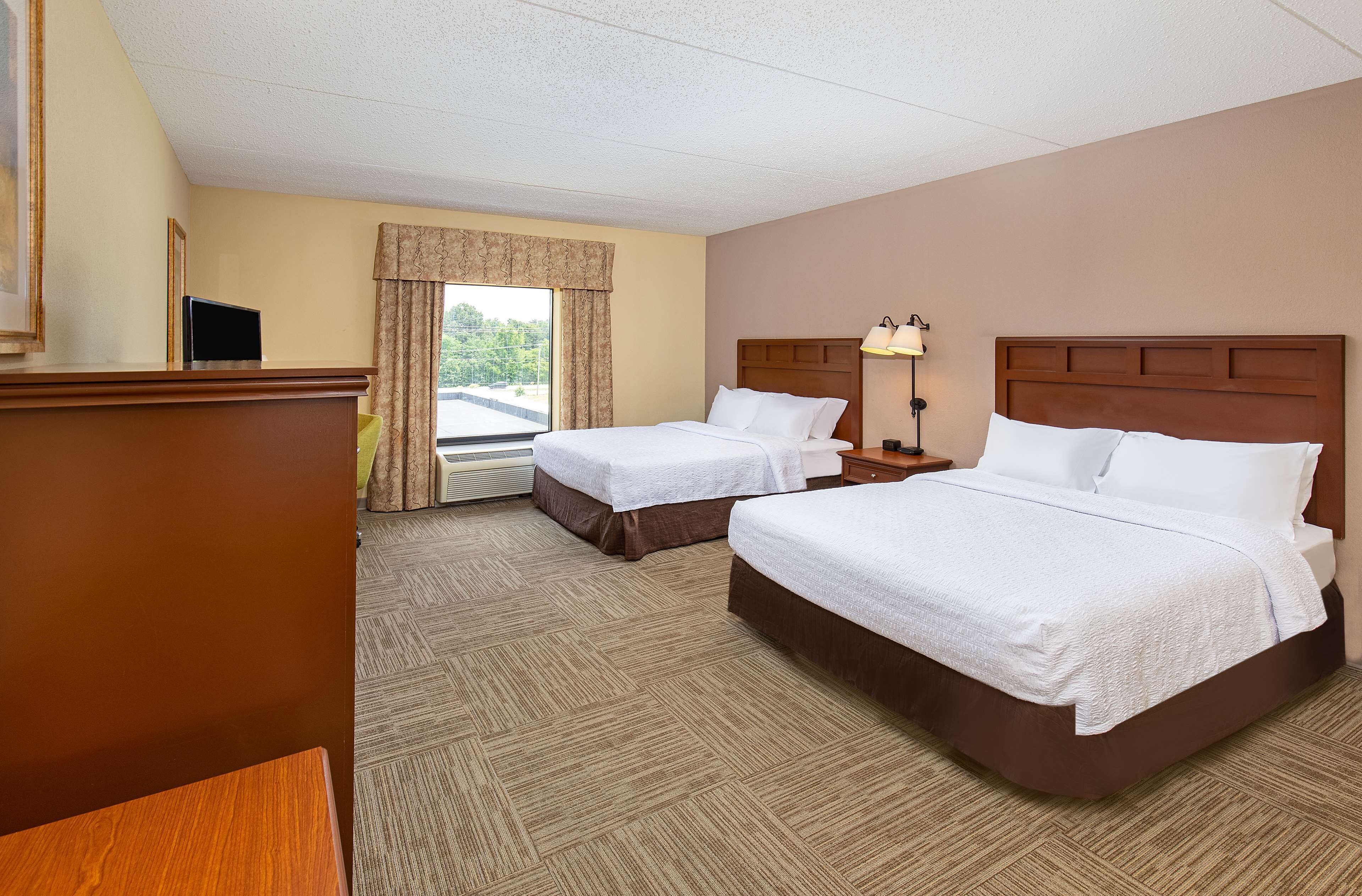 A hotel room with two beds, a desk, a lamp, and a window with curtains.