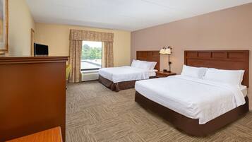 A hotel room with two beds, a desk, a lamp, and a window with curtains.