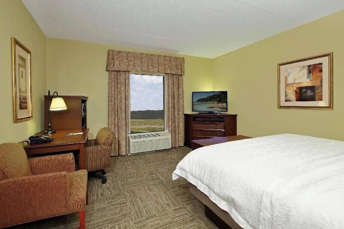 A hotel room with a bed, desk, chair, television, and a window with curtains.
