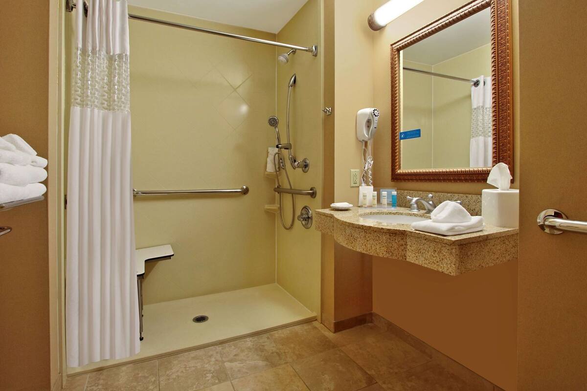 A hotel bathroom with a shower, toilet, sink, and towel rack.