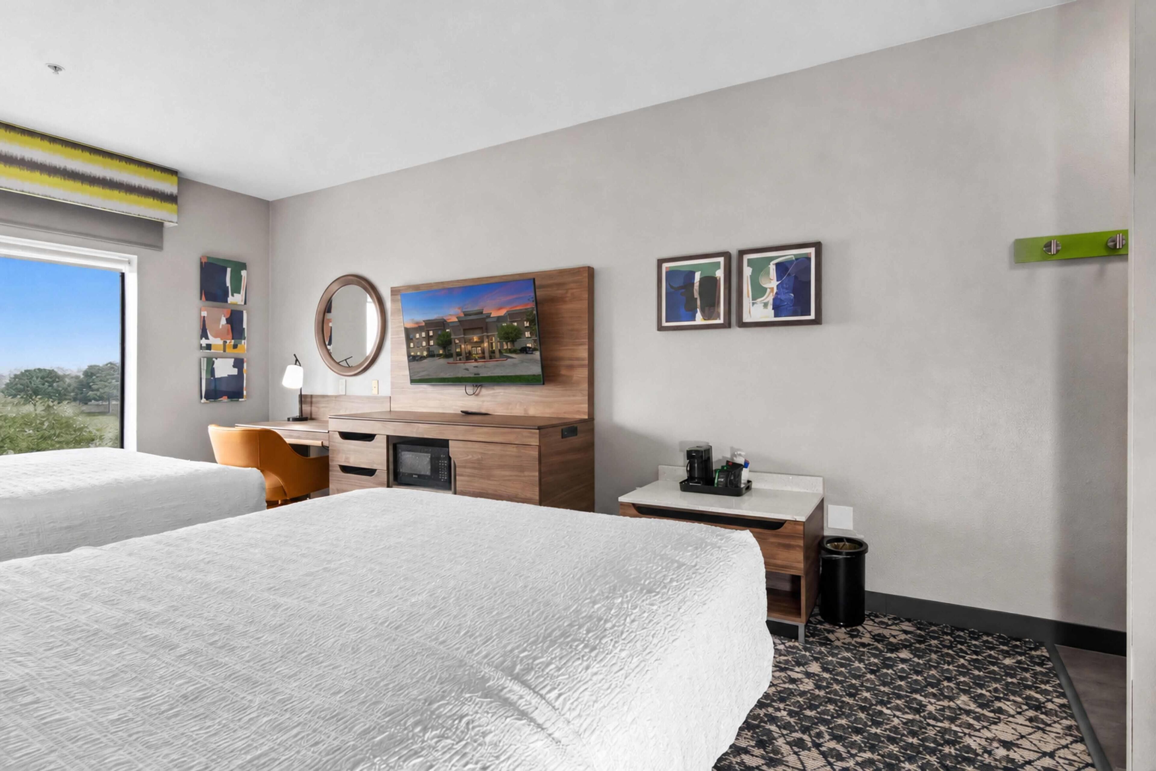 Habitación de hotel con dos camas, un escritorio, un espejo y obras de arte en la pared.