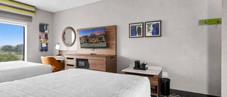 Habitación de hotel con dos camas, un escritorio, un espejo y obras de arte en la pared.