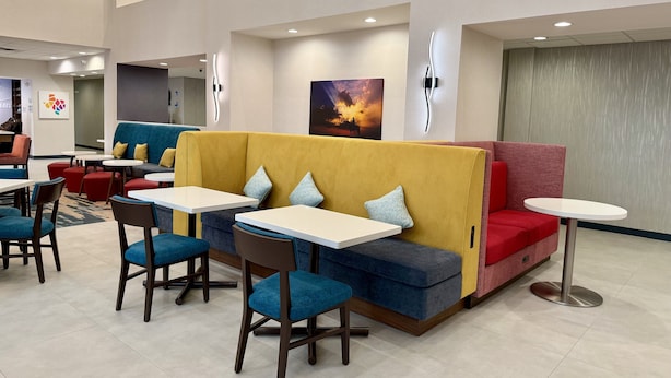 A modern dining area with booths and tables, featuring a mix of blue and red seating, and a painting on the wall. - Hampton Inn & Suites Houston - Rosenberg (Rosenberg)