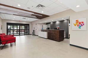 A reception area with a reception desk, a red chair, and a wall-mounted artwork. - Hampton Inn & Suites Houston - Rosenberg (Rosenberg)