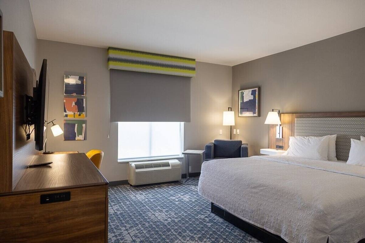 A hotel room with a large bed, a desk with a computer, a chair, a TV, and a window with a view.