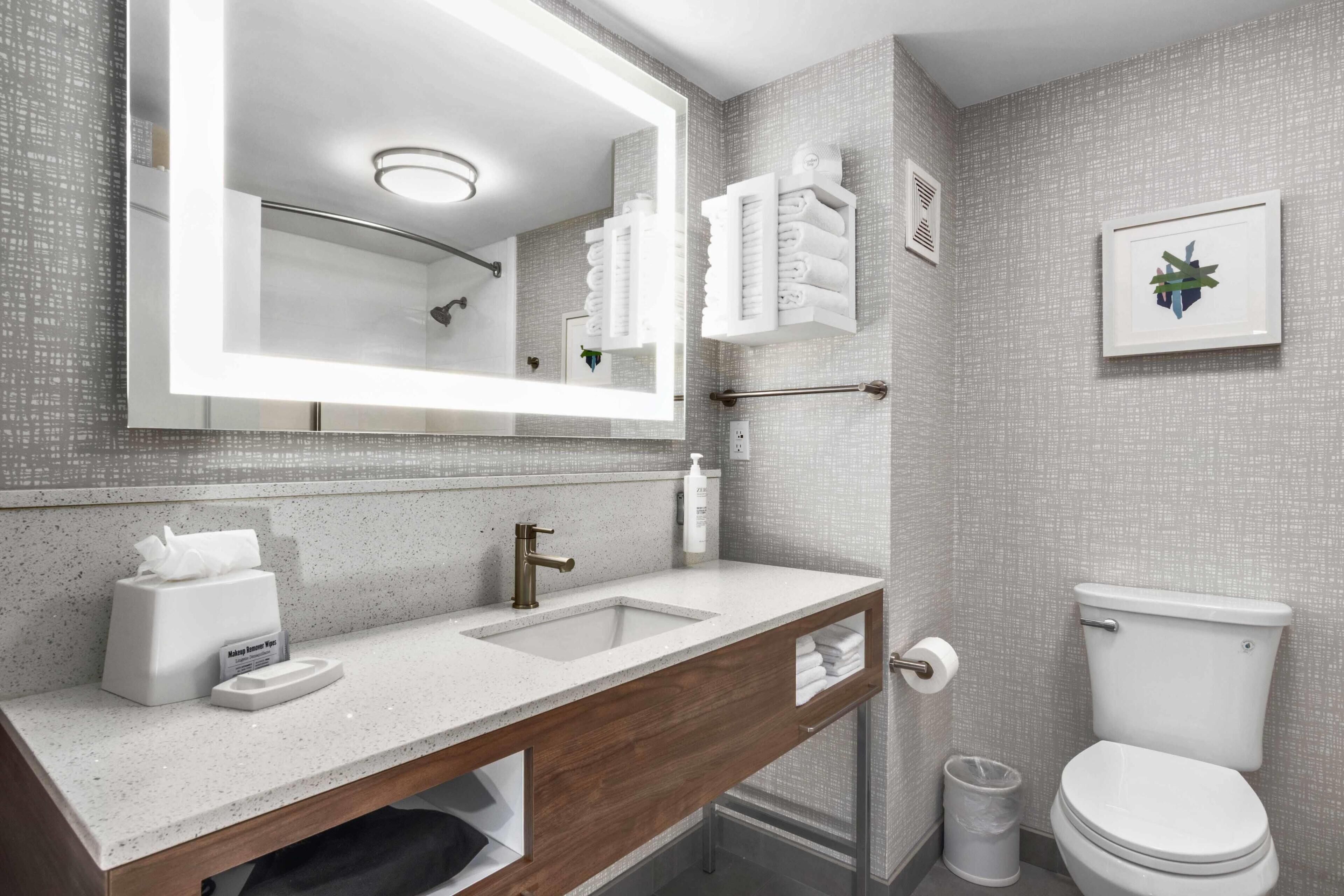 A modern bathroom with a large mirror, a sink with a towel holder, a toilet, and a shower area.