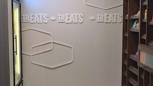 A modern interior with a wall displaying the word "TREATS" repeatedly. There is a vending machine on the left and a wooden shelving unit on the right. - Hampton Inn & Suites Houston - Rosenberg (Rosenberg)