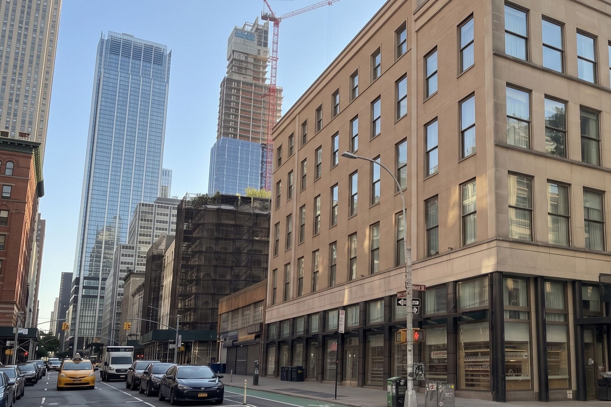 A city street with tall buildings, a taxi, and parked cars.