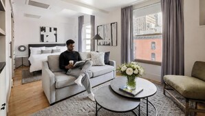 A modern hotel room with a bed, a sofa, a coffee table with flowers, and a city view. - Duane Street Hotel Tribeca, Belvilla District 6 Formerly Sonder (New York)