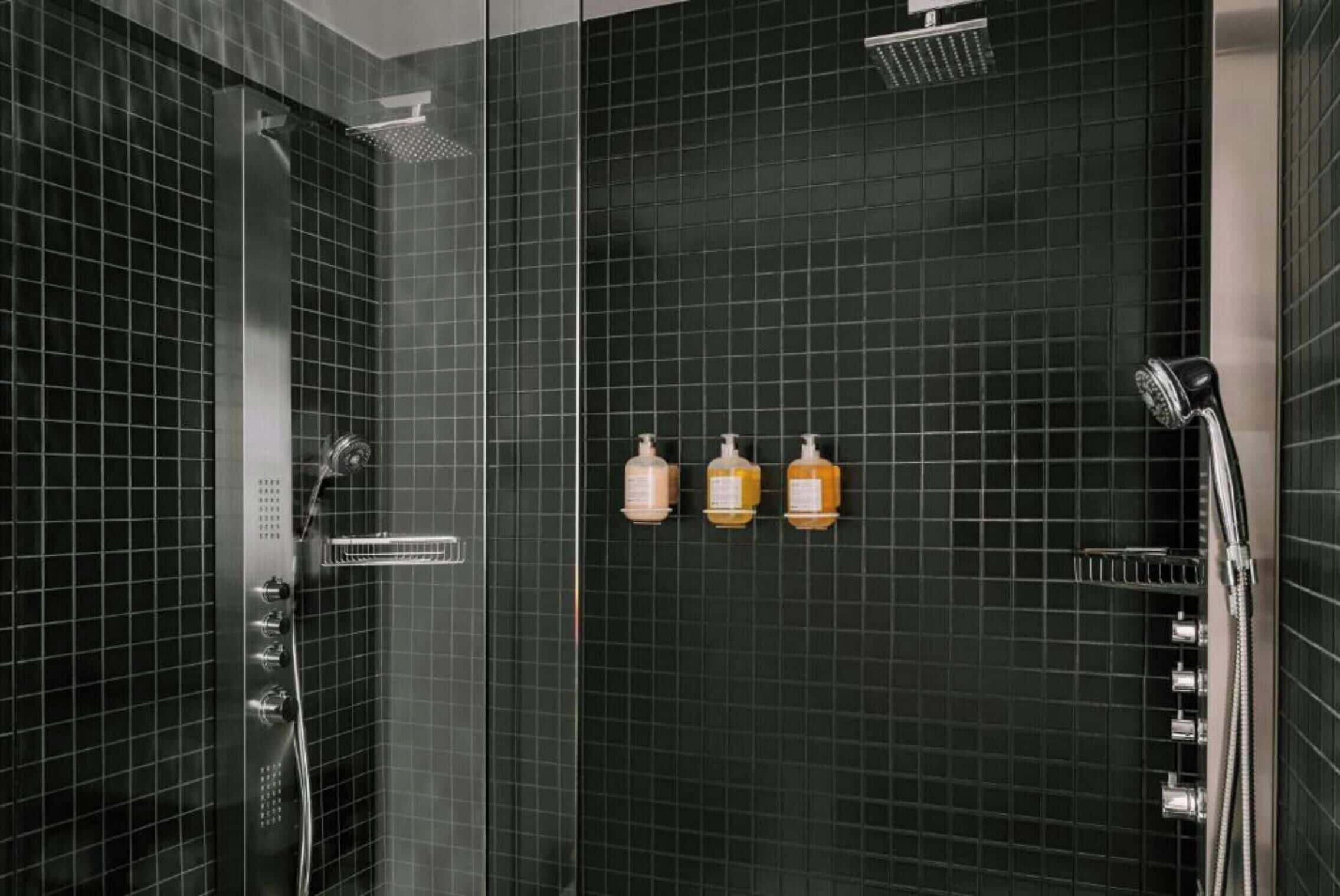 A modern shower with a glass door, a handheld showerhead, and three bottles of shampoo and conditioner on the wall.