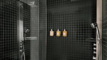 A modern shower with a glass door, a handheld showerhead, and three bottles of shampoo and conditioner on the wall.