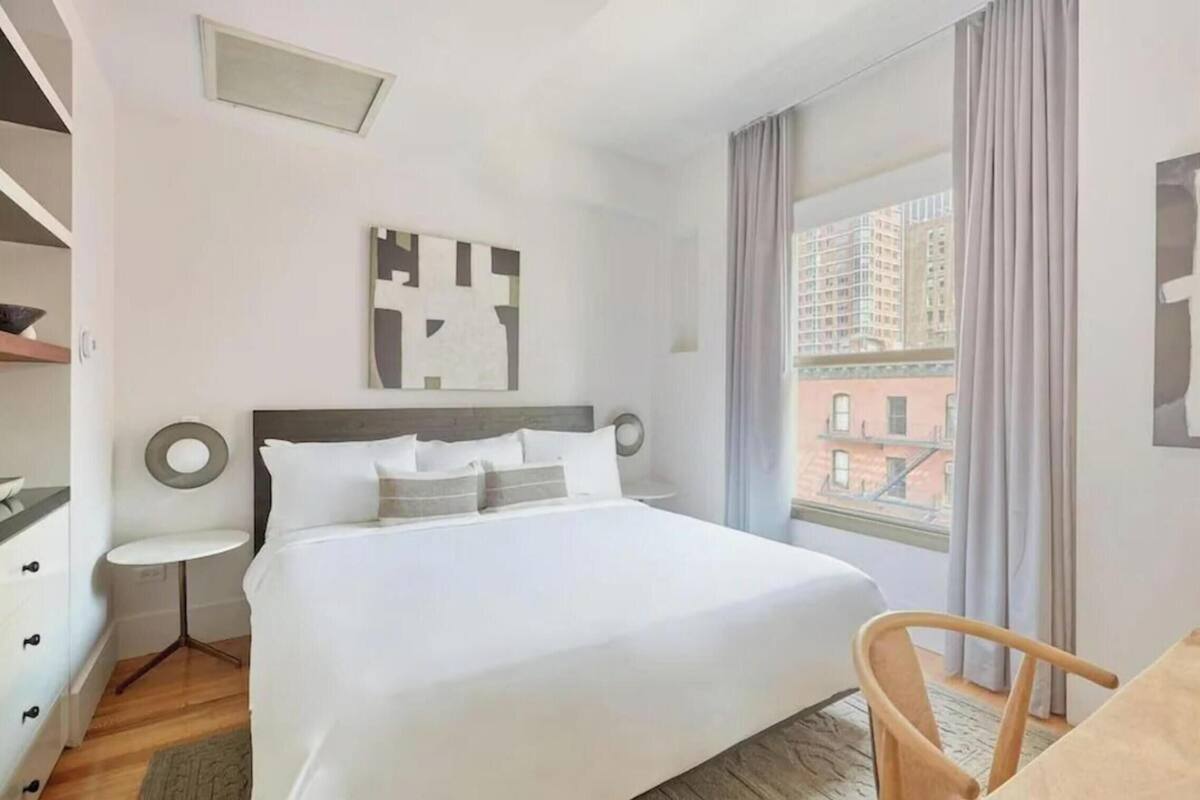 Une chambre d’hôtel avec un lit, une petite table ronde, une chaise, une fenêtre avec des rideaux et une vue sur la ville.