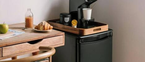 A kitchenette with a coffee machine, a croissant, a bottle of juice, and a green apple on a wooden table.
