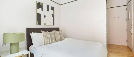 Une chambre d’hôtel moderne avec un grand lit, une table de chevet avec une lampe et une œuvre d’art murale au style minimaliste.