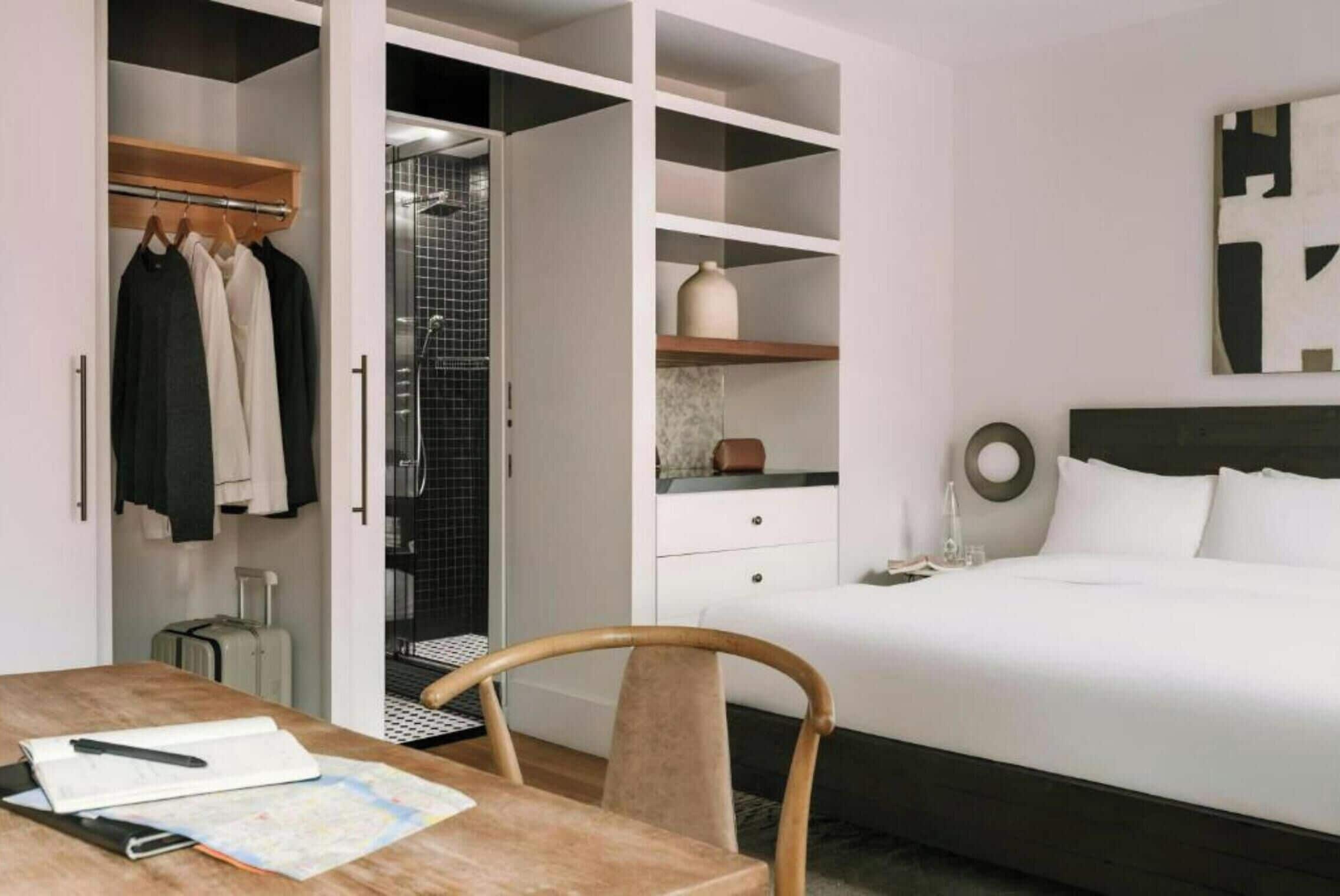 Una camera d'albergo con un letto, una scrivania con una sedia, un armadio e un bagno con doccia.