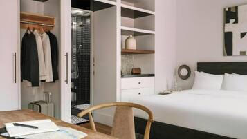 Una camera d'albergo con un letto, una scrivania con una sedia, un armadio e un bagno con doccia.