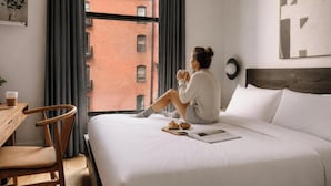 A hotel room with a bed, a chair, a table, a window with curtains, and a view of buildings outside. - Duane Street Hotel Tribeca, Belvilla District 6 Formerly Sonder (New York)