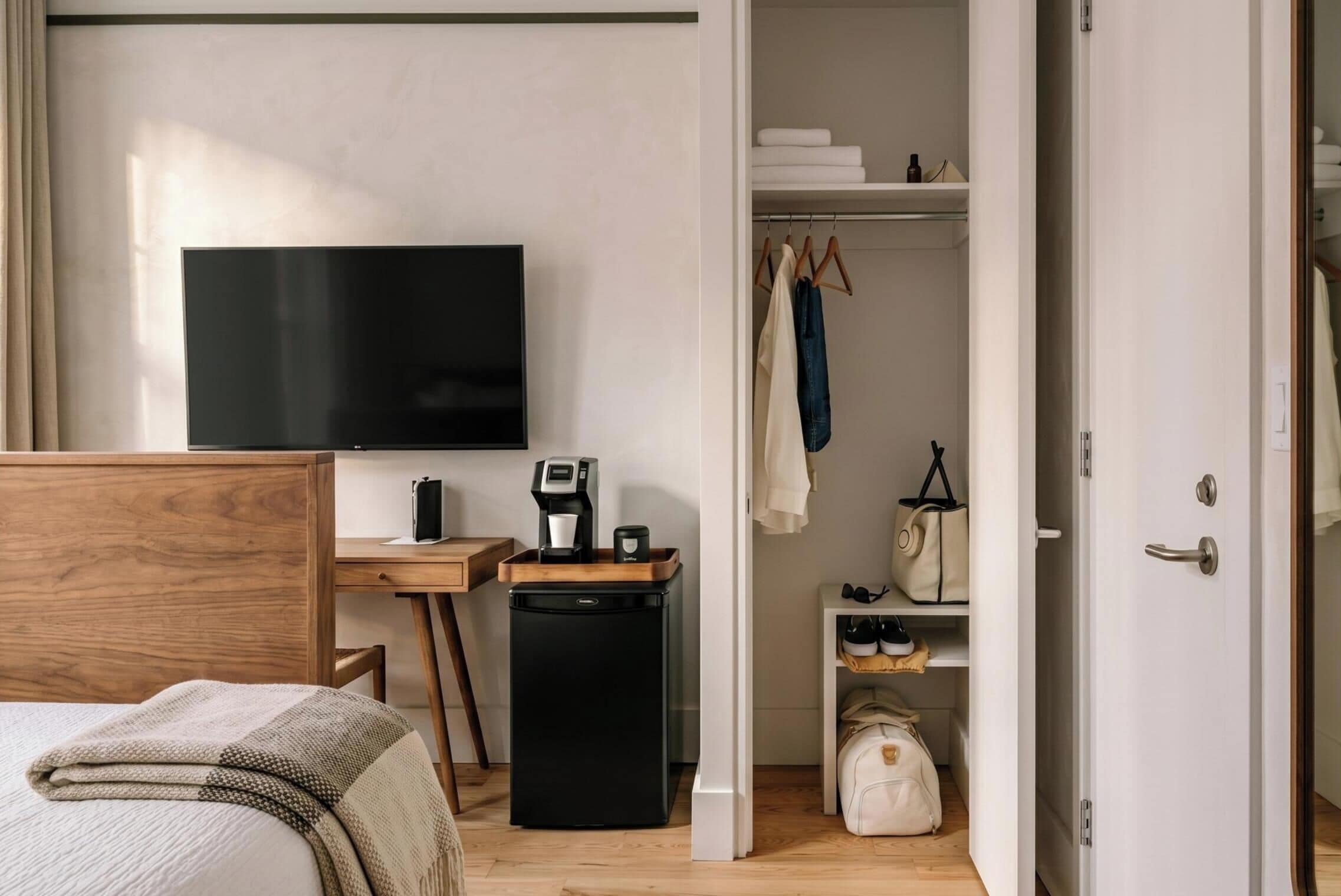 A bedroom with a bed, a desk with a TV, a coffee machine, and a wardrobe.