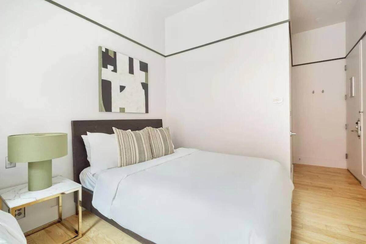 Une chambre d’hôtel moderne avec un grand lit, une table de chevet avec une lampe, une œuvre d’art murale et un plancher en bois.