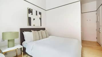 A modern hotel room with a large bed, a nightstand with a lamp, a wall art piece, and a wooden floor.
