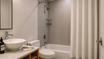 Un baño con lavamanos, inodoro, bañera, cortina de ducha y espejo en la pared.