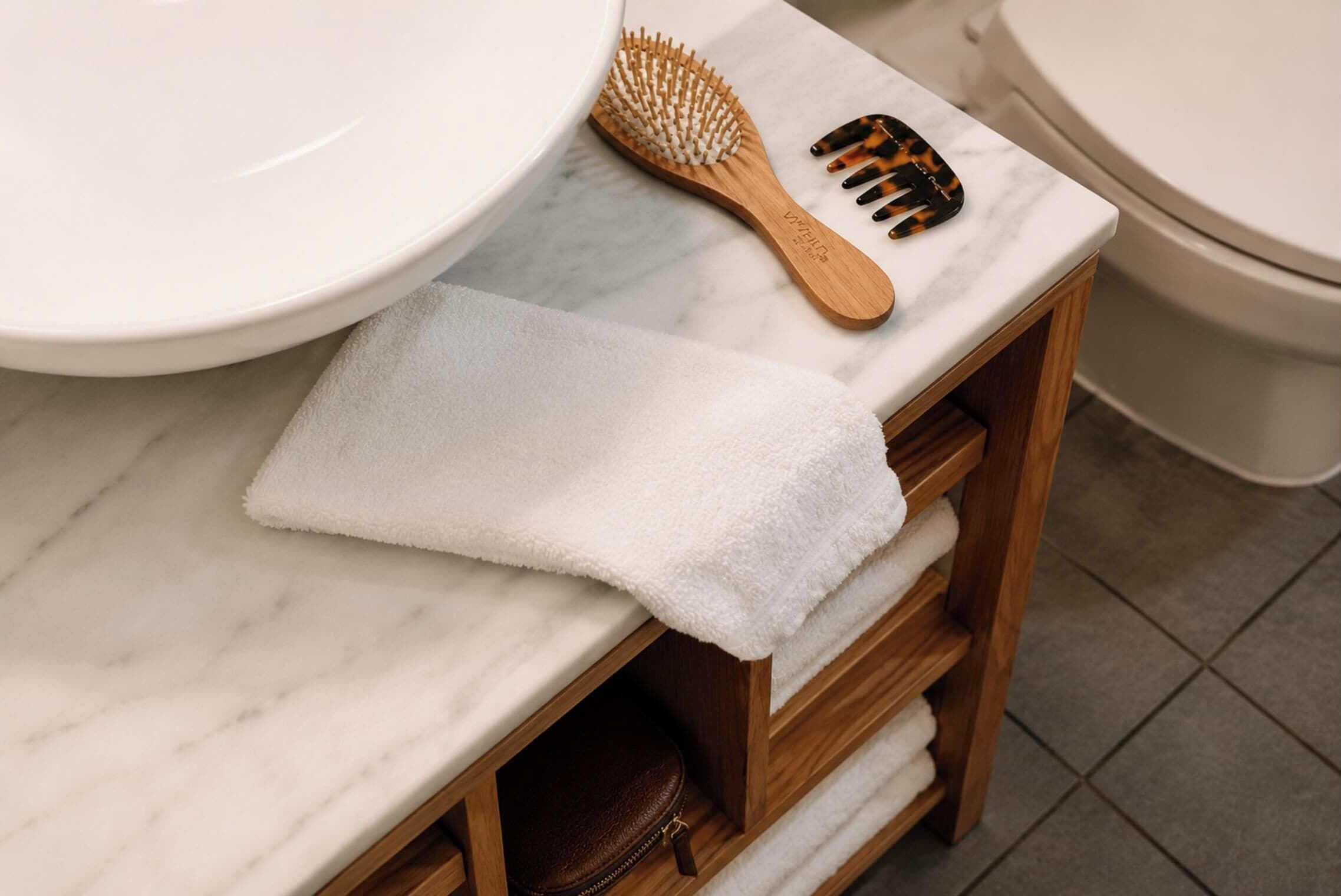 Une salle de bain avec un lavabo en marbre, des étagères en bois, une serviette, une brosse en bois et un peigne.