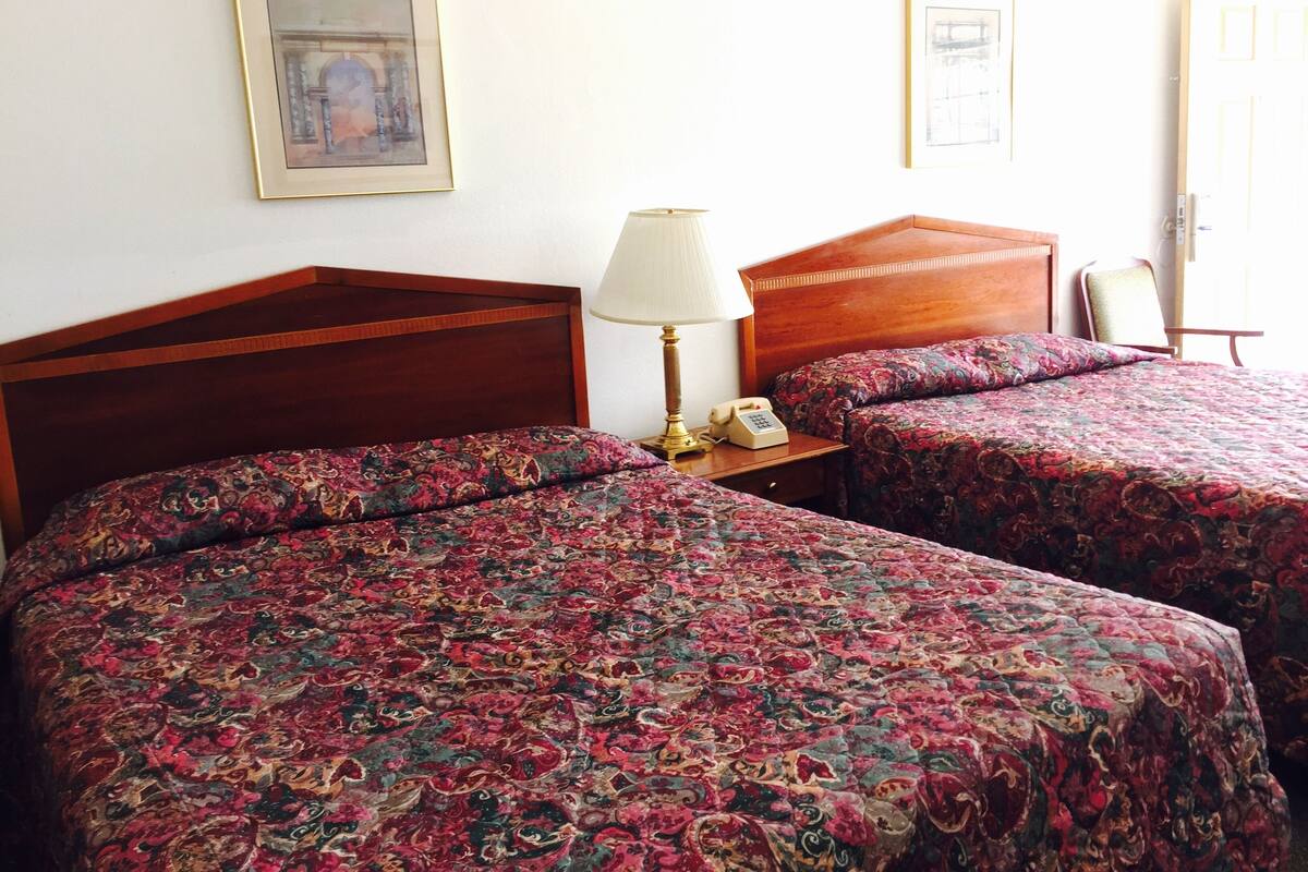 Une chambre d’hôtel avec deux lits, une lampe de chevet, un téléphone et des tableaux encadrés au mur.