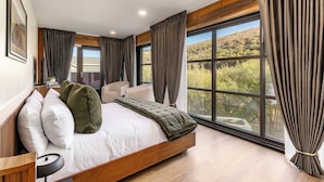 Un dormitorio con un ventanal grande, una cama con almohadas, una mesita de noche y una silla.