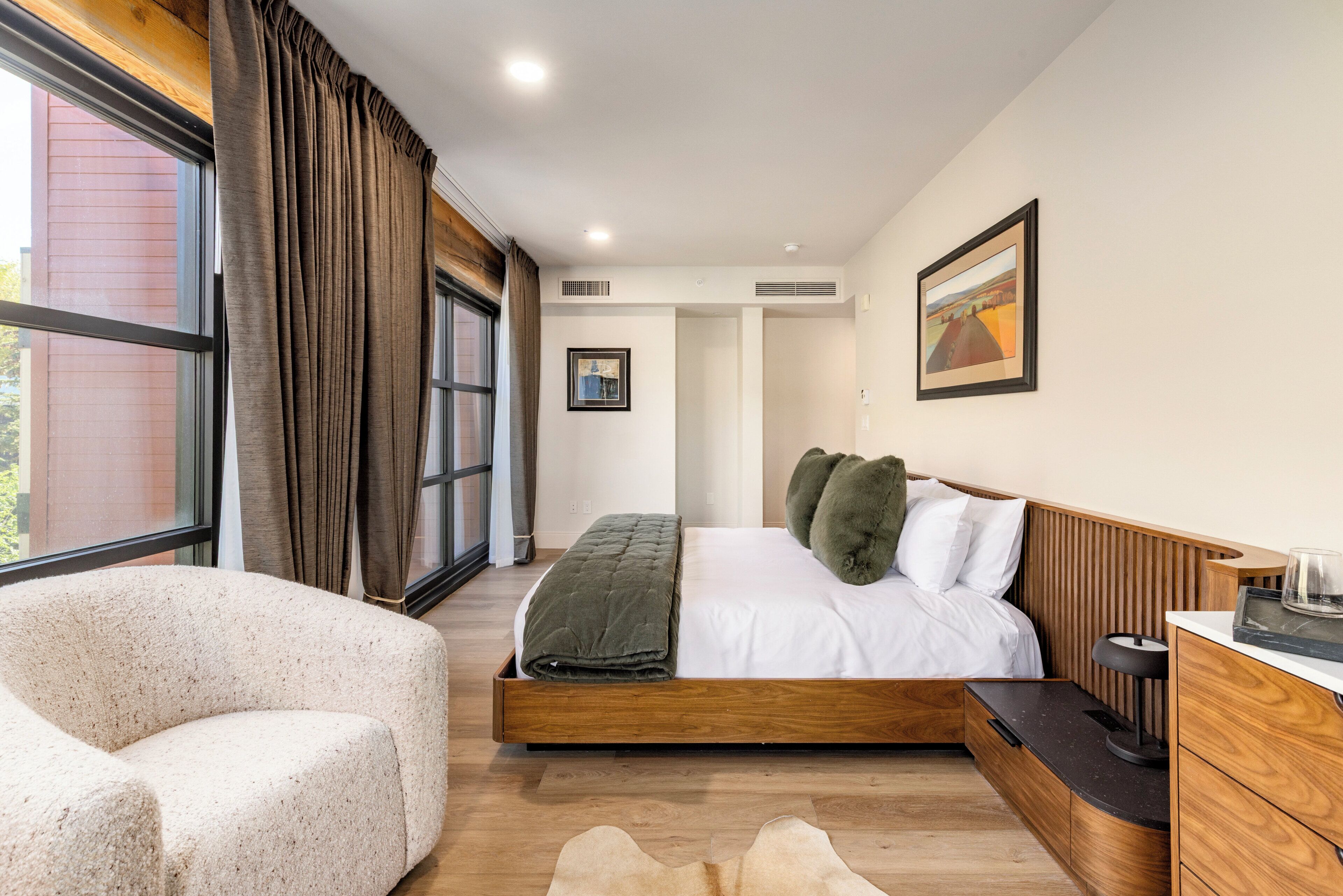 A bedroom with a bed, a chair, a bedside table, and a window with curtains.