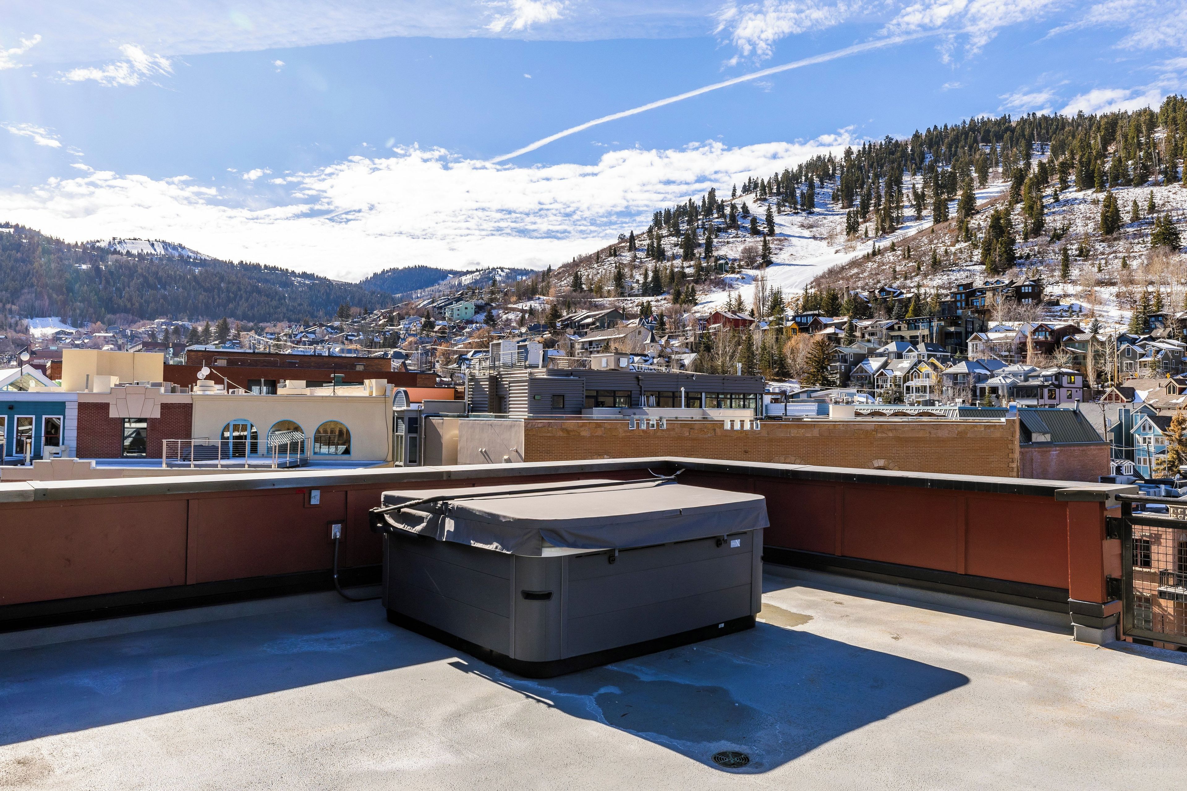 A rooftop with a large, dark-colored storage unit, a clear sky, and a view of a snow-covered town with buildings and trees.