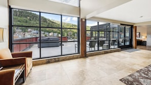 Un amplio salón con grandes ventanales que ofrecen vistas a una ladera y casas vecinas.