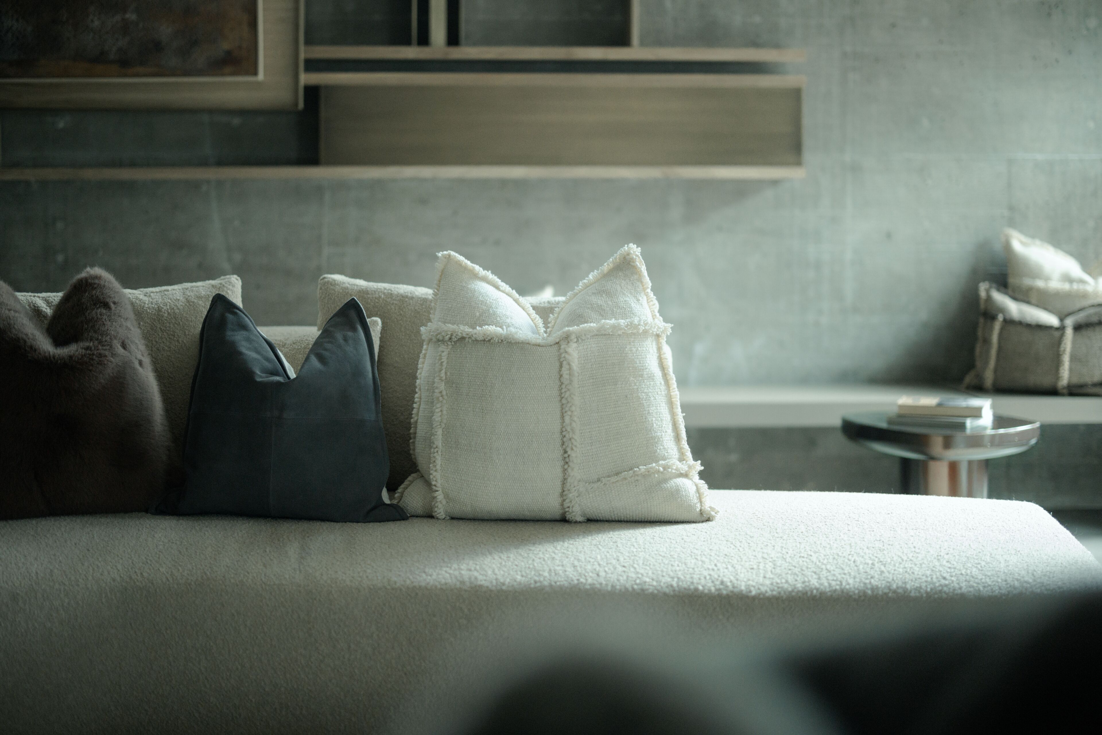 A bed with pillows, a small round table, and a wall-mounted shelf.