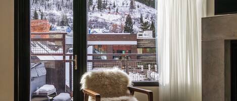 Una habitación con vista a una montaña nevada, una chimenea y un sillón junto a la ventana.